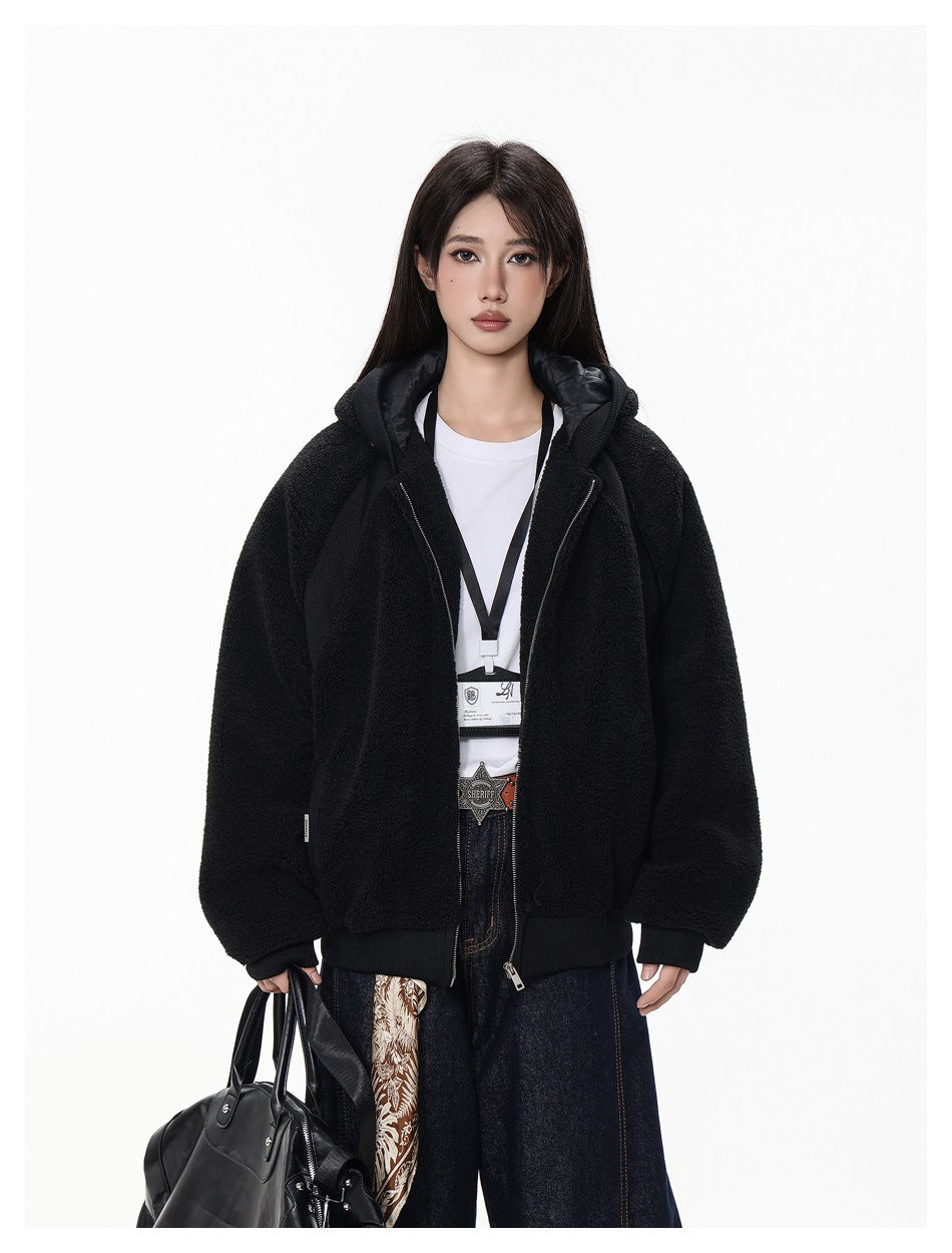 Model wearing open black hooded fleece-style jacket over a white tee with dark wide-leg jeans, holding a black bag