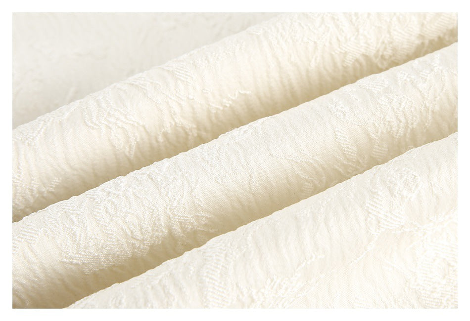 Macro view of the raised floral texture on ivory fabric arranged in soft folds.
