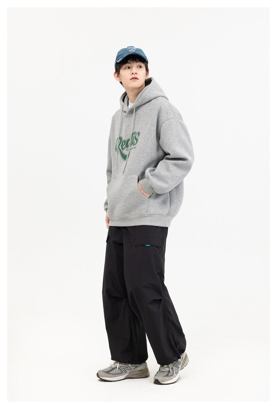 Model in a gray pullover hoodie with a green chest graphic and black cargo pants, shown at an angle.