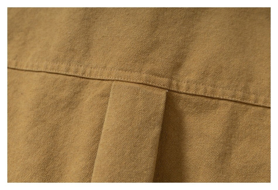 Close-up of mustard-brown garment stitching and a narrow fabric tab.