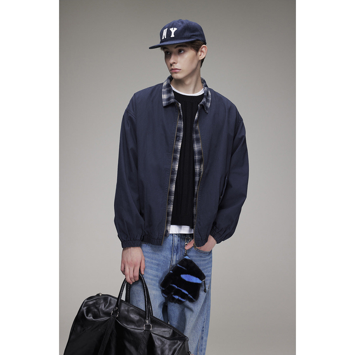 Model wearing a navy zip-front jacket with plaid trim, layered over a black sweater and plaid shirt.