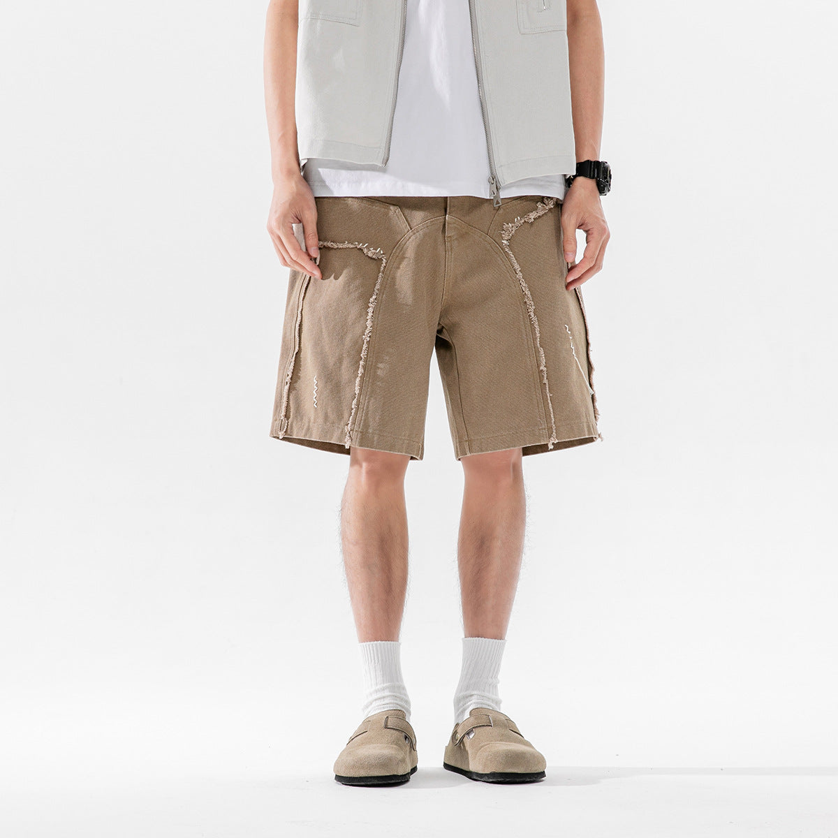 Front view of a model wearing taupe shorts with curved frayed panel seams and a light vest.