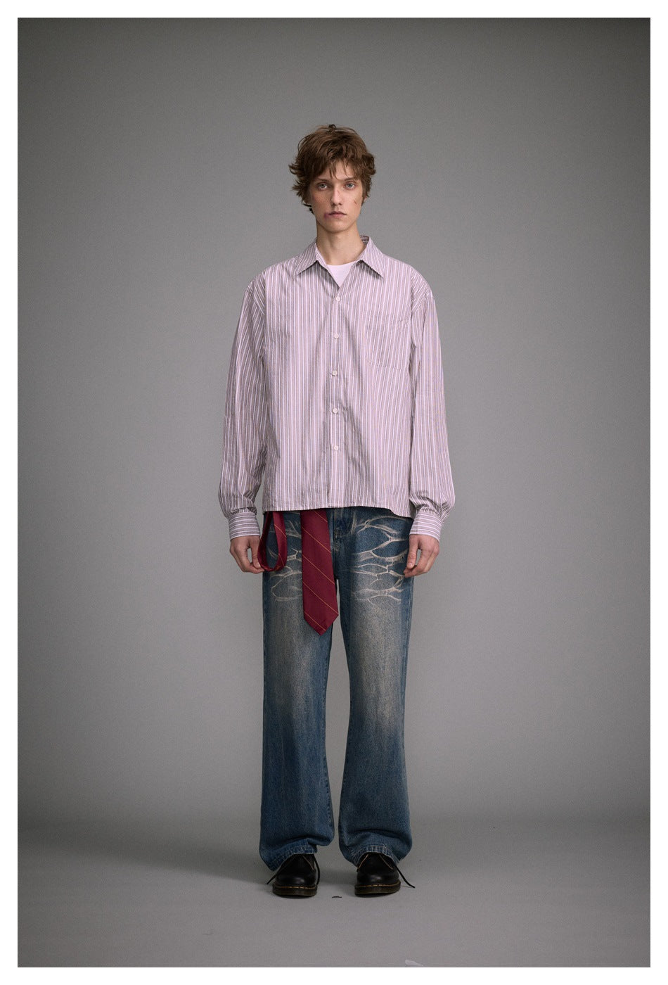 Full-length front view of a model in a loose pink-and-white striped button-up shirt and wide blue jeans.
