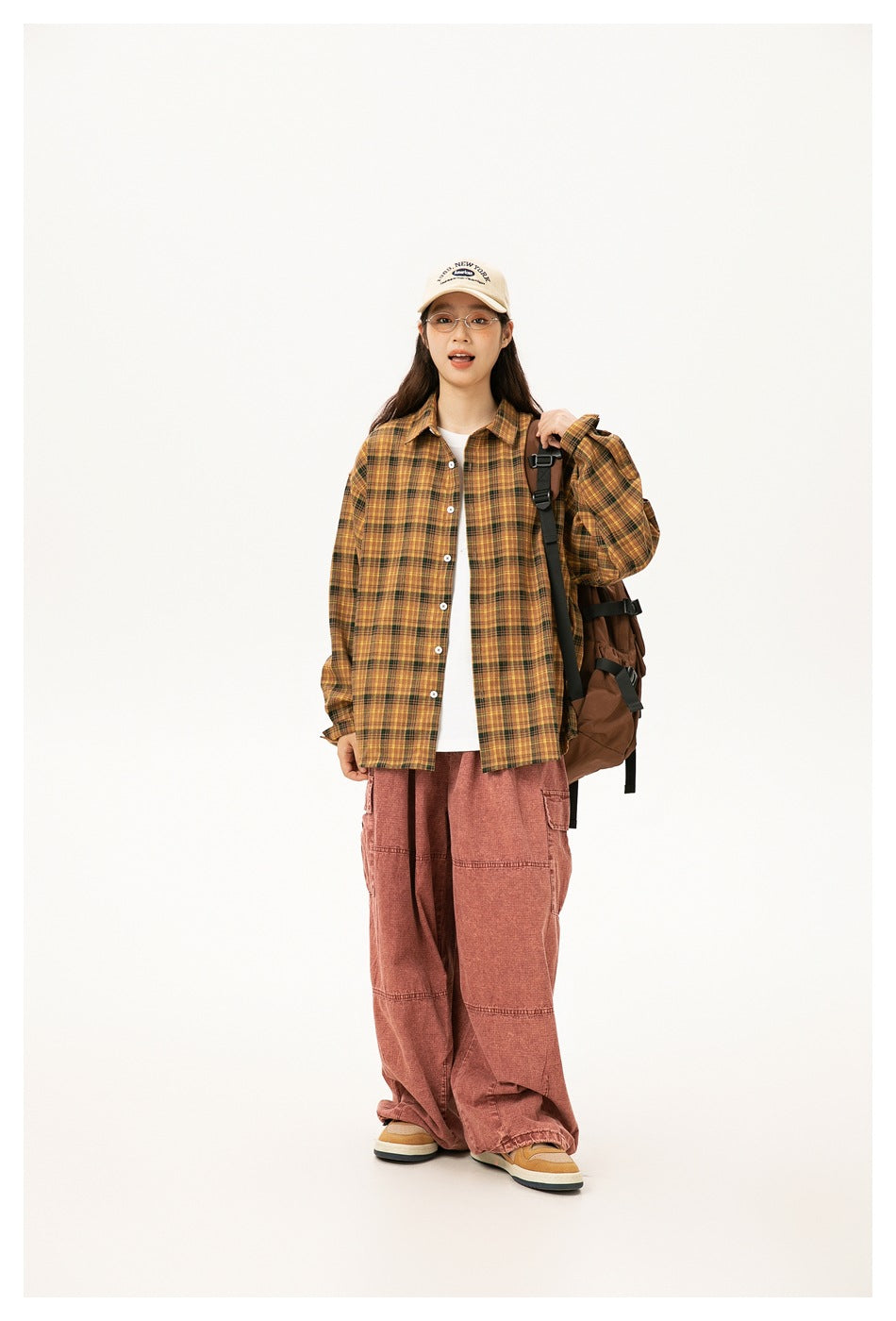 A model wears a mustard yellow plaid button-up shirt over a white top with loose rose-colored pants.