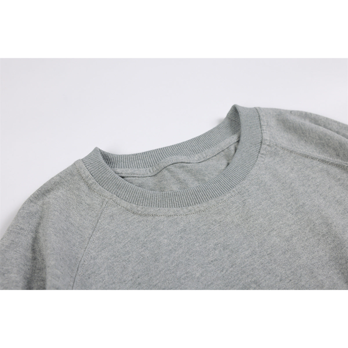 Close-up of a light gray sweatshirt's ribbed crew neckline and shoulder seam.