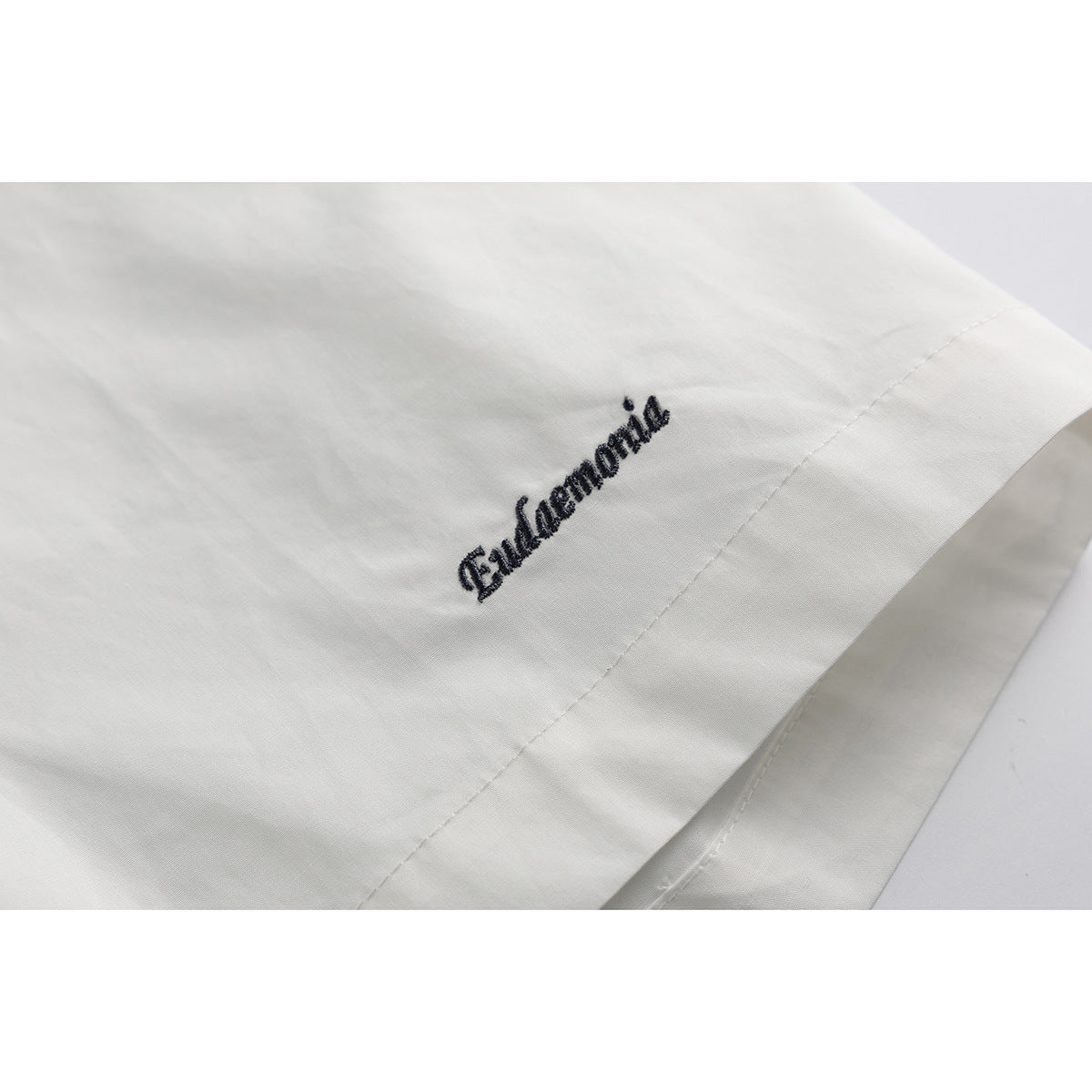 Close-up of dark cursive embroidery near the hem of a white shirt.
