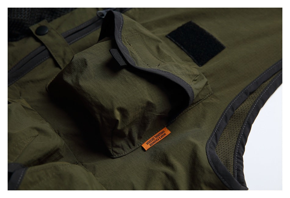 Close-up of an olive vest flap pocket, hook-and-loop patch and orange garment tag.
