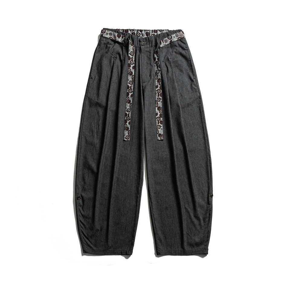 Dark charcoal-black wide-leg trousers flat lay with a paisley-print tie belt and button tabs at the hems