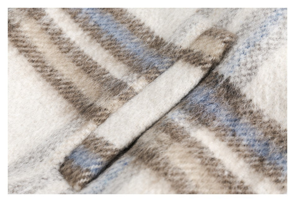 Close-up of a narrow cream fabric tab against the garment's cream, taupe, and pale blue plaid.