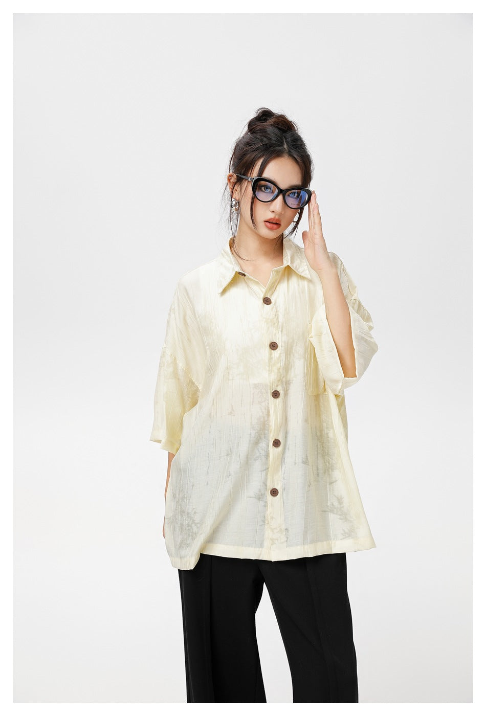 Model wearing an oversized ivory patterned button-up shirt with short sleeves, a chest pocket, and black trousers.