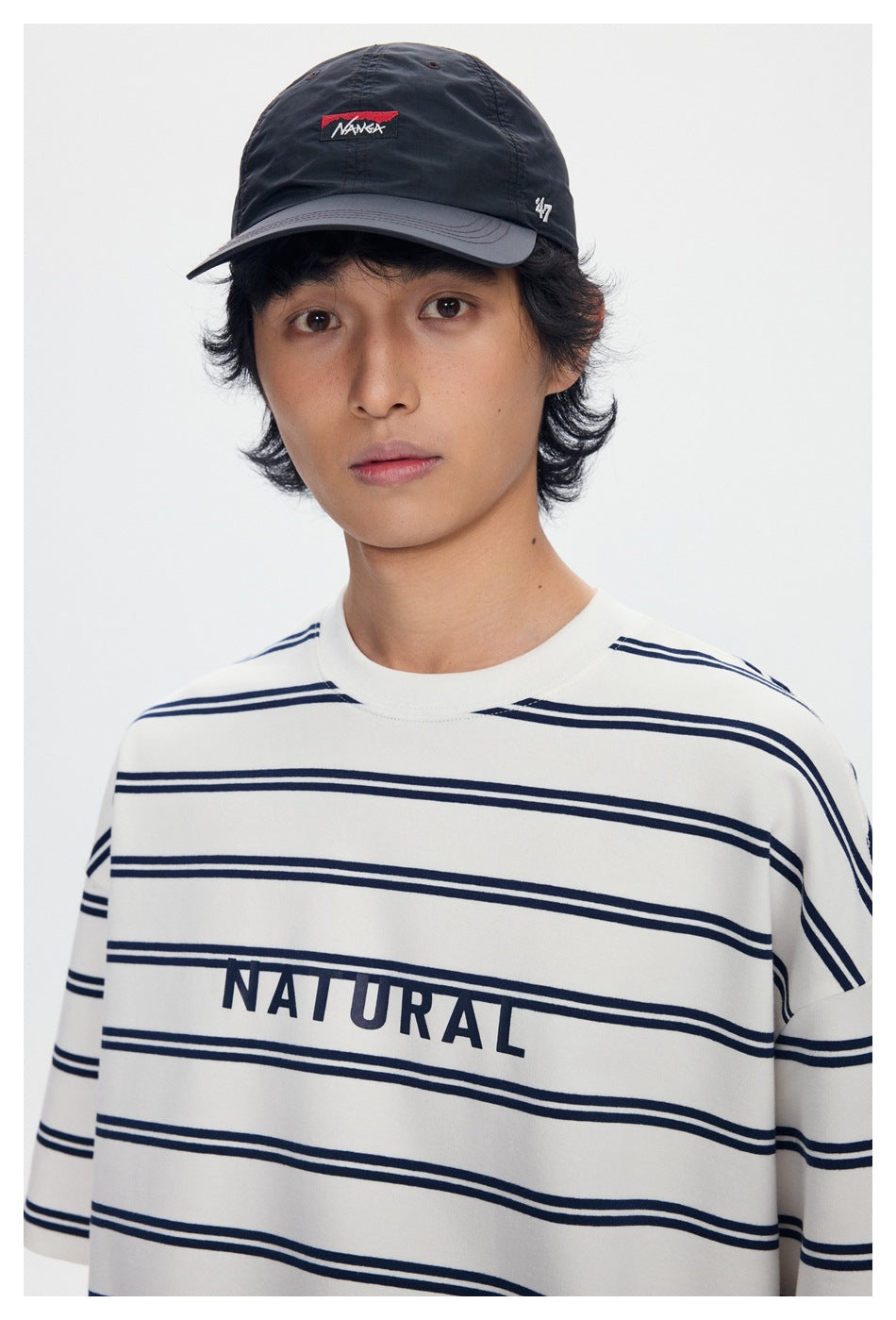 Close view of the striped ivory T-shirt's chest lettering and neckline, with the model wearing a black cap.