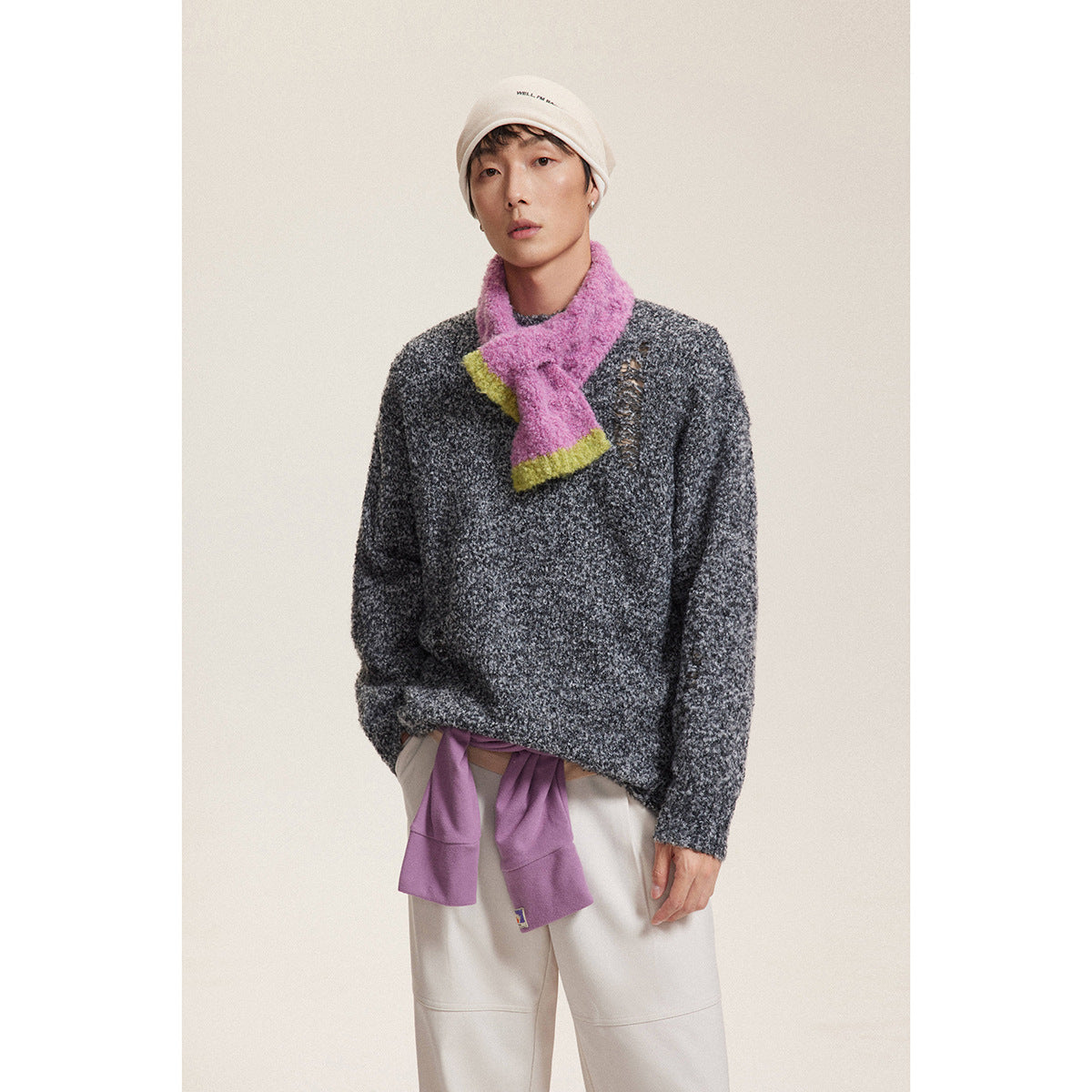 Model wearing a charcoal marled crewneck sweater with distressed detailing, a pink scarf, and light trousers.