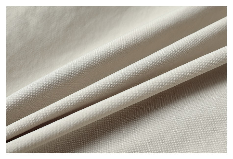 Close-up of light beige fabric arranged in overlapping folds, showing its fine surface texture.