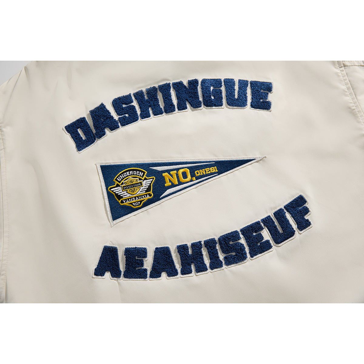 Close-up of the ivory jacket back, showing arched navy embroidery and a blue-and-gold pennant patch.