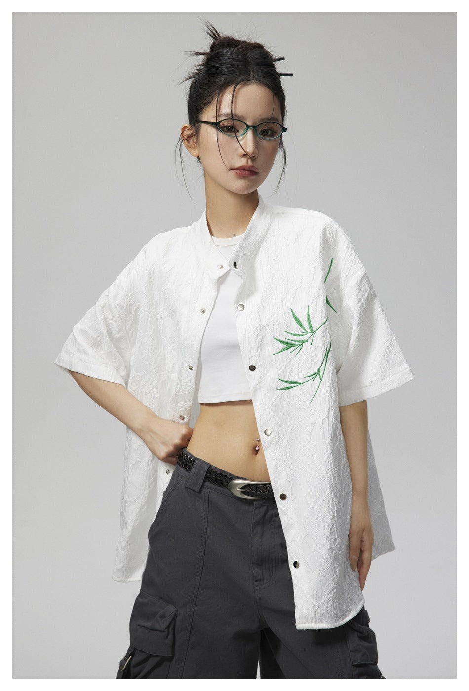 Model wearing an oversized white textured short-sleeve button-up with green branch embroidery.