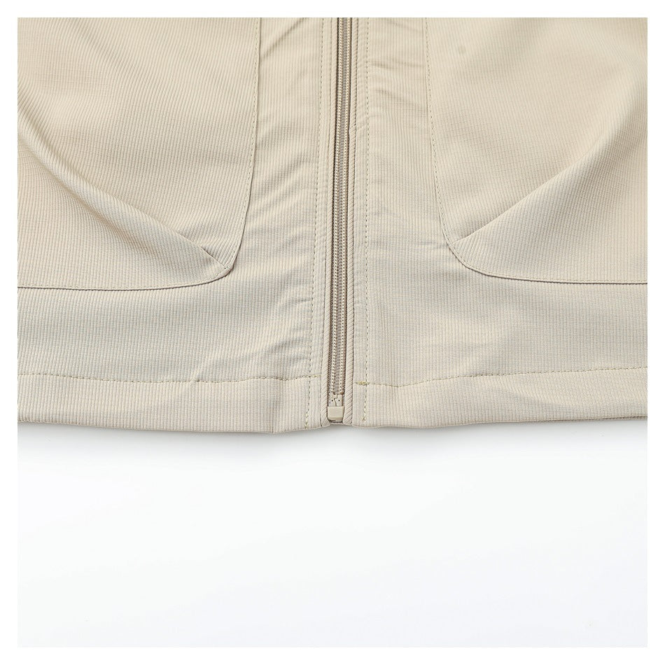 Close-up of a beige jacket front showing the center zipper, lower hem, and curved pocket edges.