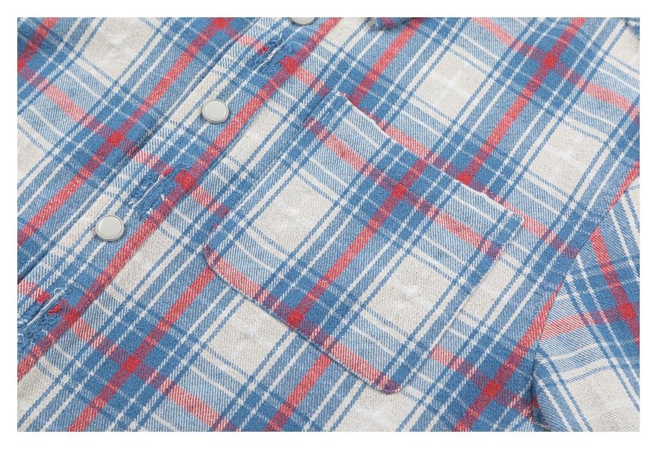 Close-up of a square chest pocket and snap-button placket on a blue, red, and cream plaid shirt.