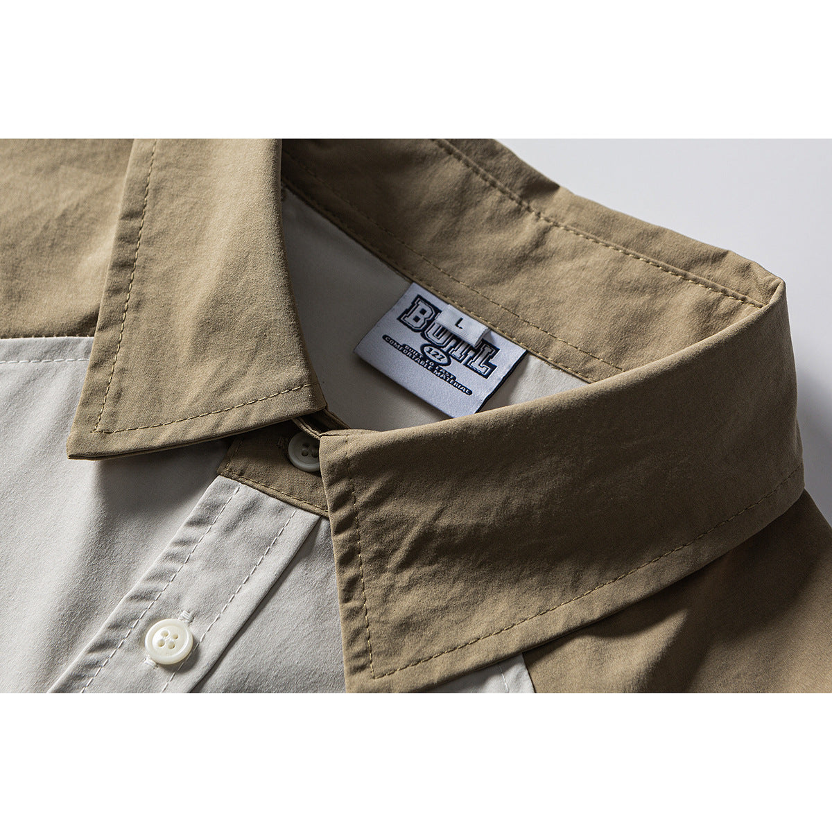 Close-up of a khaki shirt collar, cream button placket, stitching, and sewn neck label.