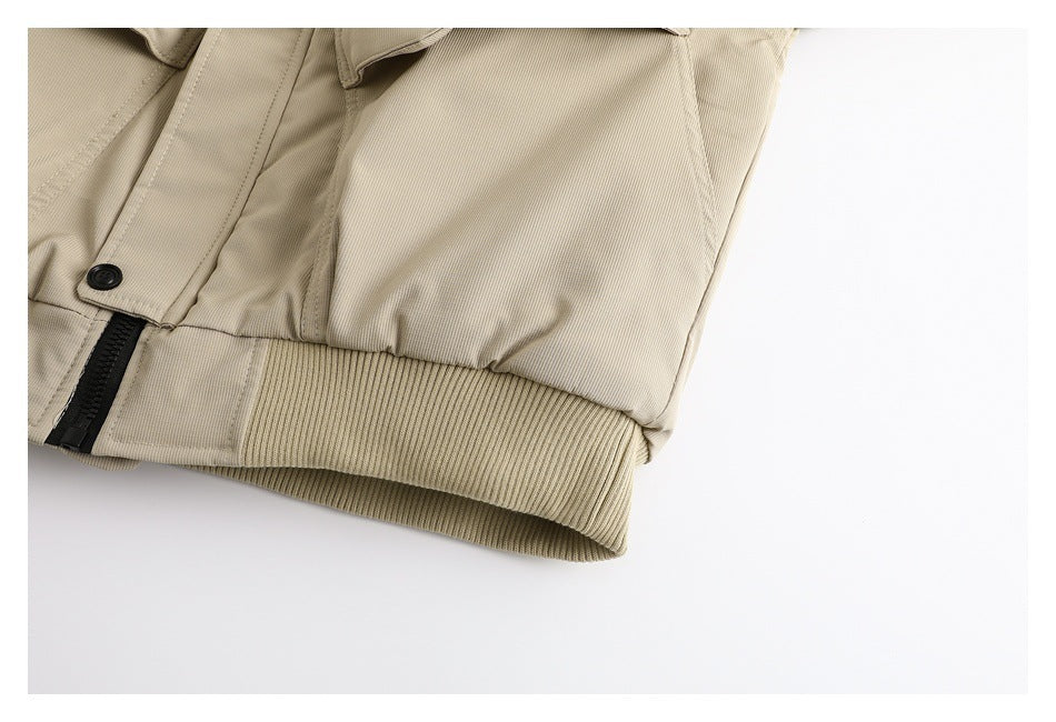 Close-up of the beige jacket's ribbed hem, black zipper, and snap-fastened flap.
