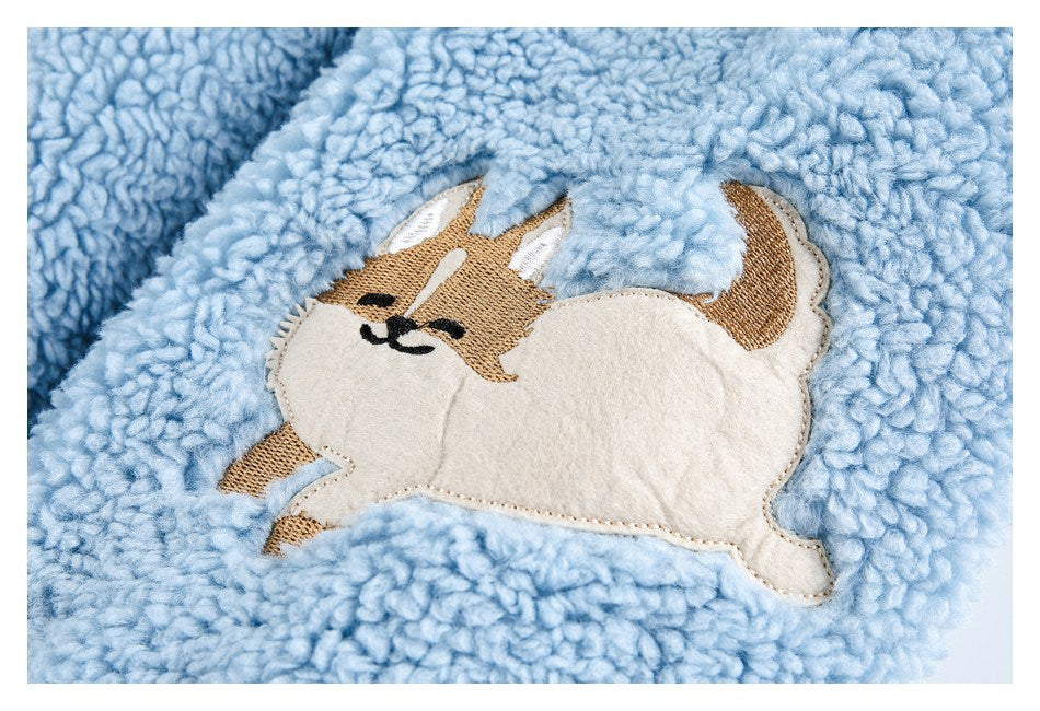 Close-up of a tan and cream dog appliqué on light blue plush fabric.