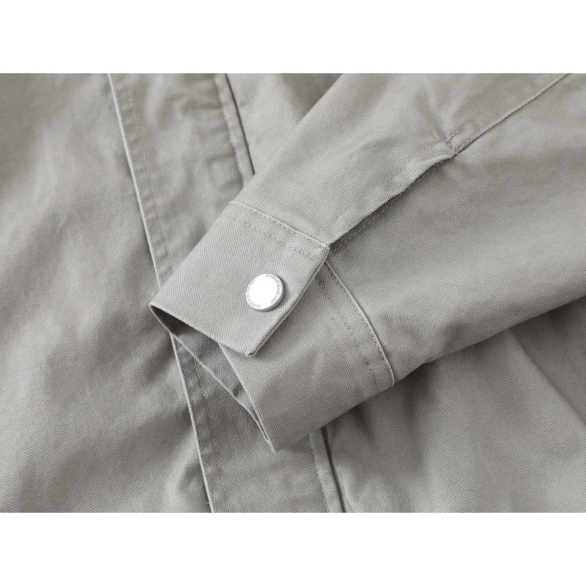 Close-up of a light gray jacket cuff with a round button and visible seam details.