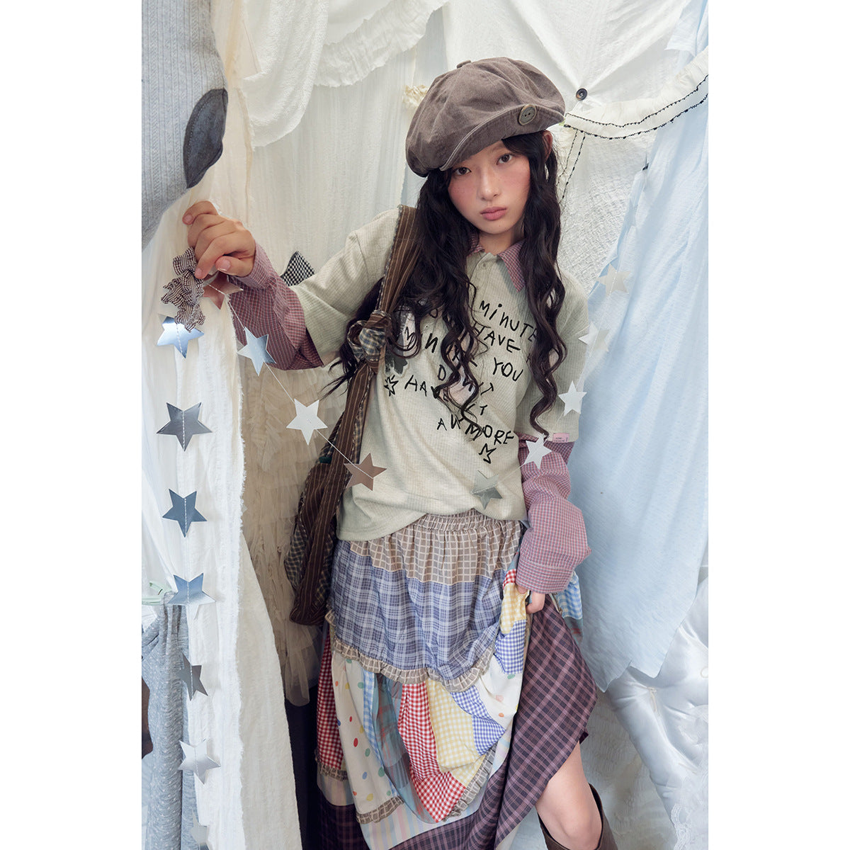 Model wearing a cream graphic top with red checked layered sleeves and a colorful patchwork skirt.