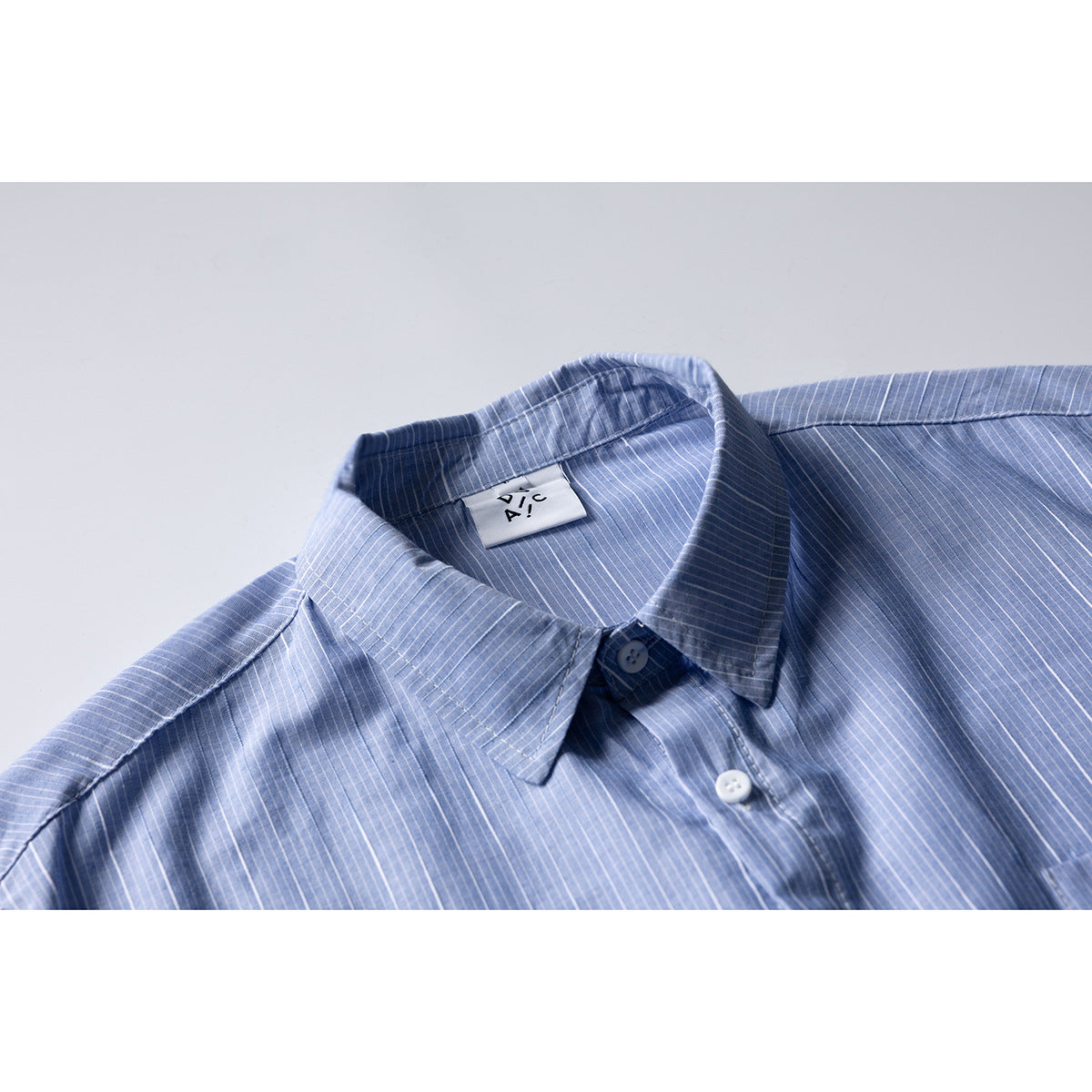 Close-up of a light blue pinstriped shirt showing its pointed collar, white button, and neck label.