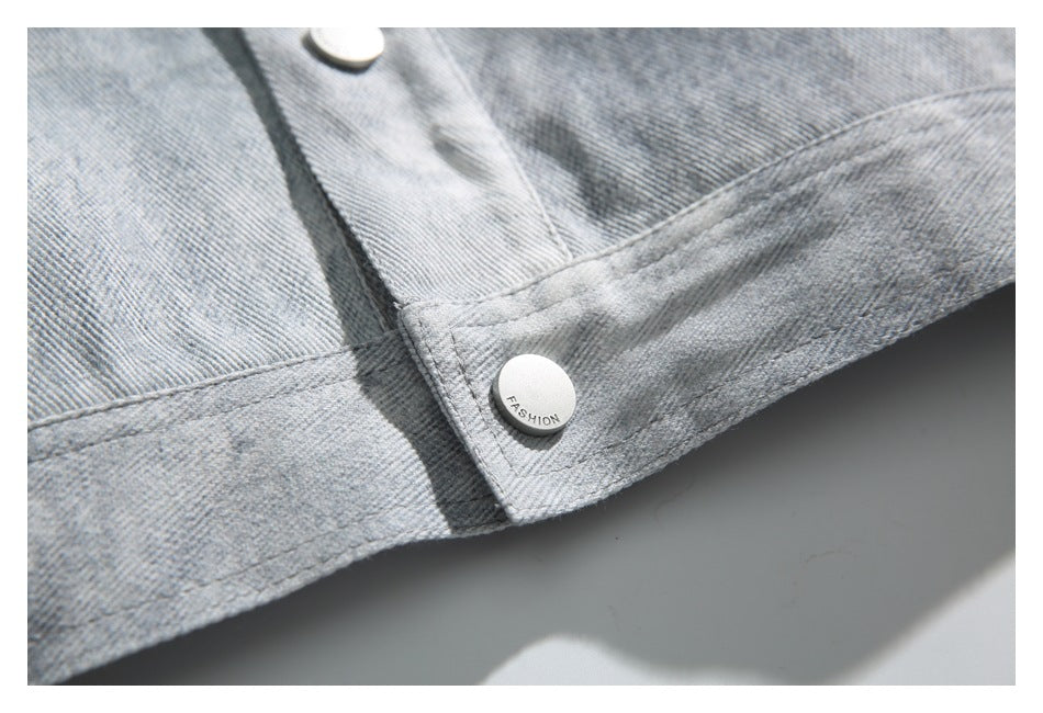 Close-up of the light gray denim jacket hem and lower button placket, with a white button marked “FASHION.”