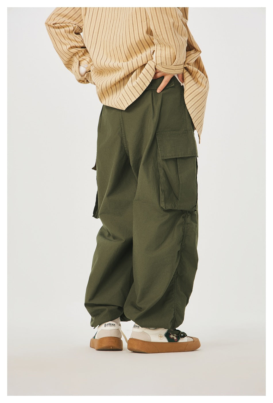 Rear view of a model wearing loose olive cargo pants with a flap pocket and gathered ankle hems.