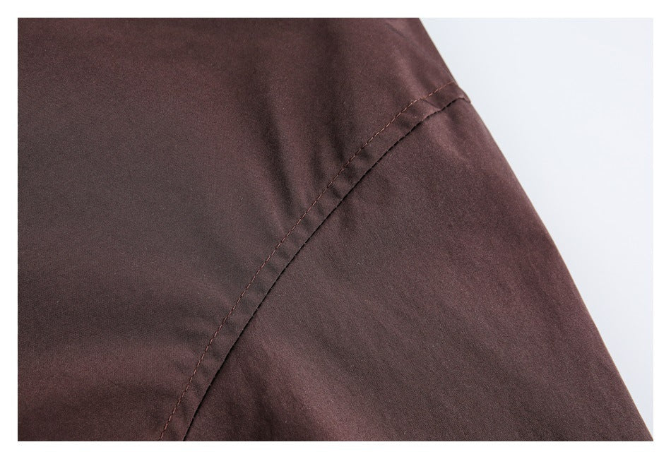 Close-up of a curved stitched seam on dark brown jacket fabric.