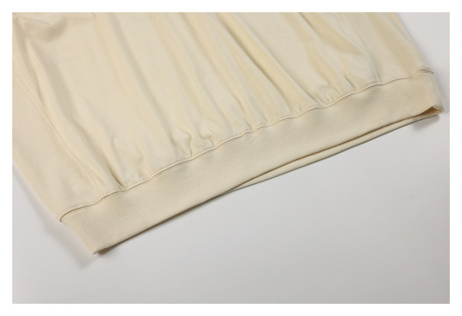 Close-up of an ivory sweatshirt’s wide ribbed hem and gathered fabric above it.