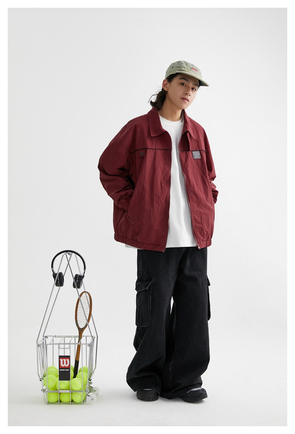 Model wearing a burgundy zip jacket with black chest piping over a white shirt, paired with loose black trousers.