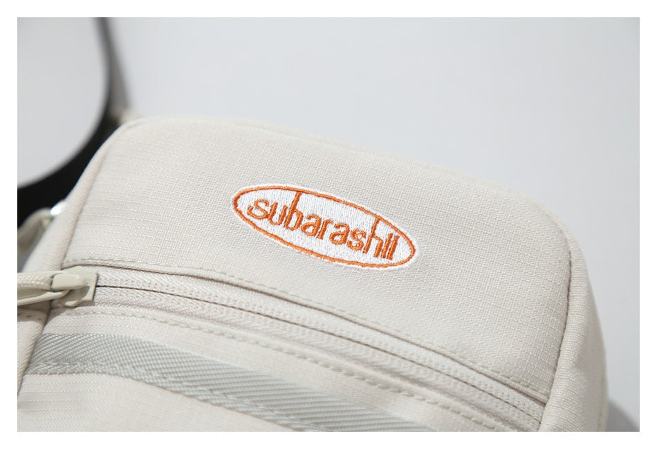 Close-up of a cream bag with an orange oval embroidered label and a zip pocket.
