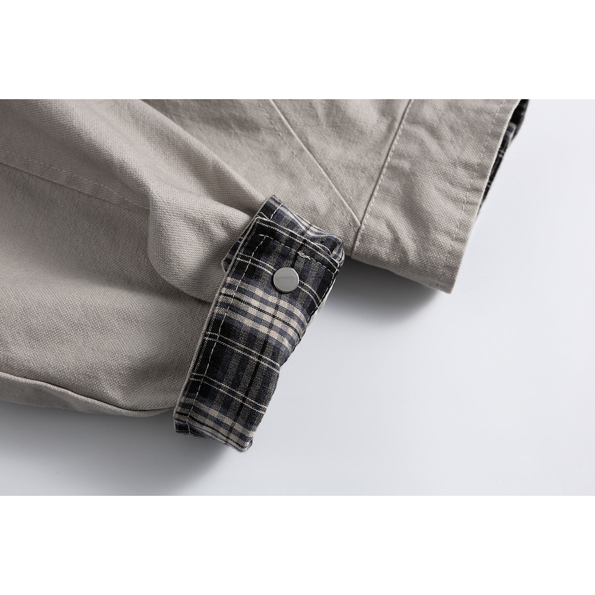 Close-up of a light gray jacket cuff with a snap tab and black plaid lining.