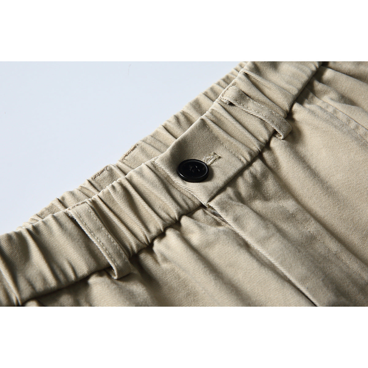 Close-up of beige trousers showing a gathered waistband, belt loops, and a black button.