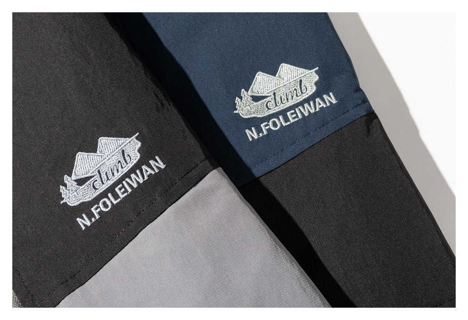 Close-up of black and navy garment panels with white embroidered ship emblems and N.FOLEMAN lettering.