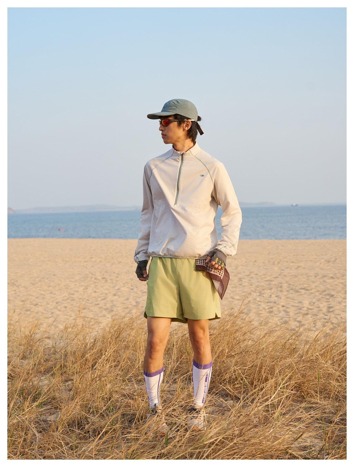 Person standing on a beach wearing lime green shorts with a light half-zip pullover, cap and tall socks
