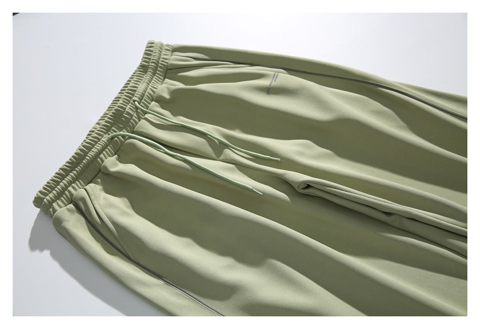 Close-up of pale sage pants showing the elastic waistband, drawstring, pocket area and dark side piping.