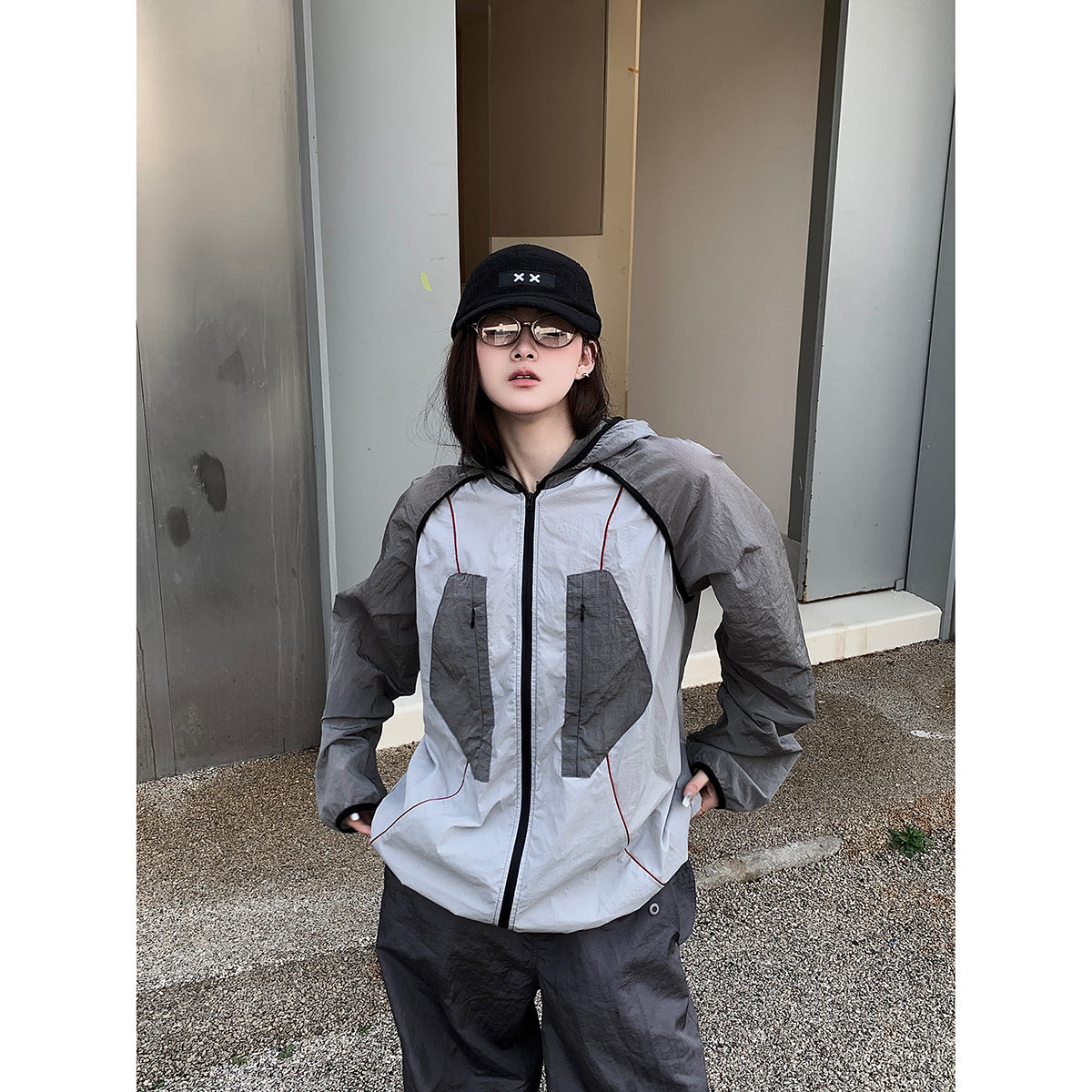 Model wearing a light gray hooded jacket with dark gray panels and loose charcoal pants, shown from the front.