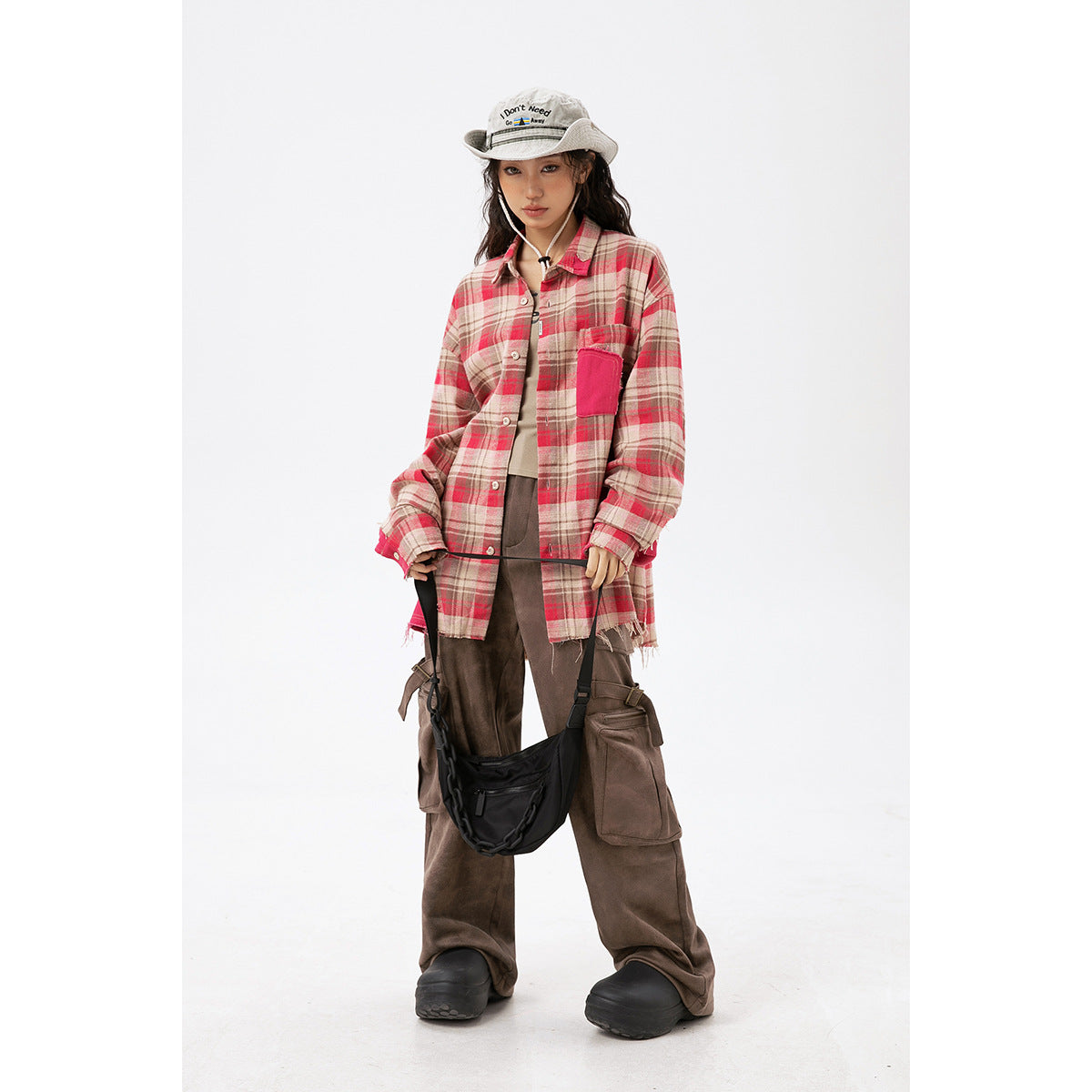 Model wearing an oversized beige and red plaid button-up shirt with a bright pink chest pocket and cuff accents.