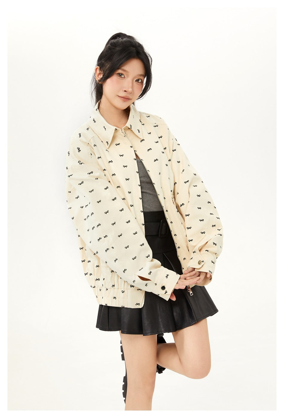 Model posing in a cream black-bow-print jacket over a gray top and black skirt; front three-quarter view.