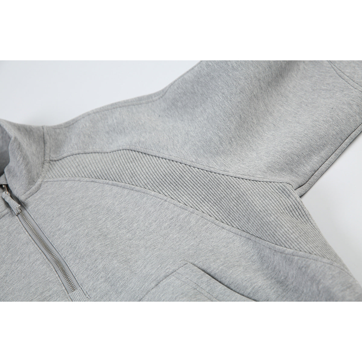 Close-up of the gray pullover's ribbed side panel, curved seams, quarter zip, and kangaroo pocket edge.