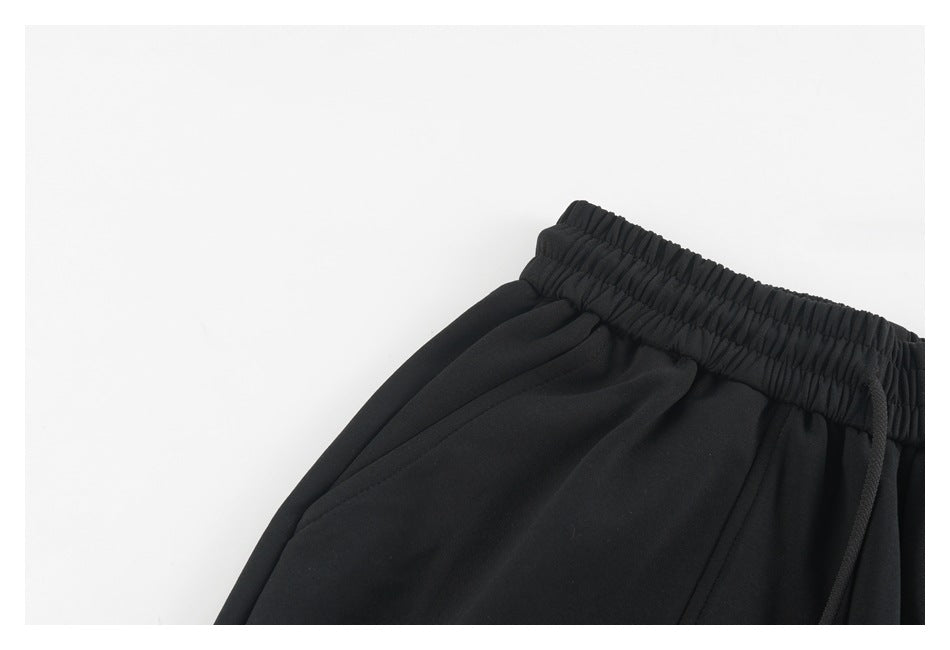 Close-up of black pants showing the gathered elastic waistband, drawstring, and front pleats.