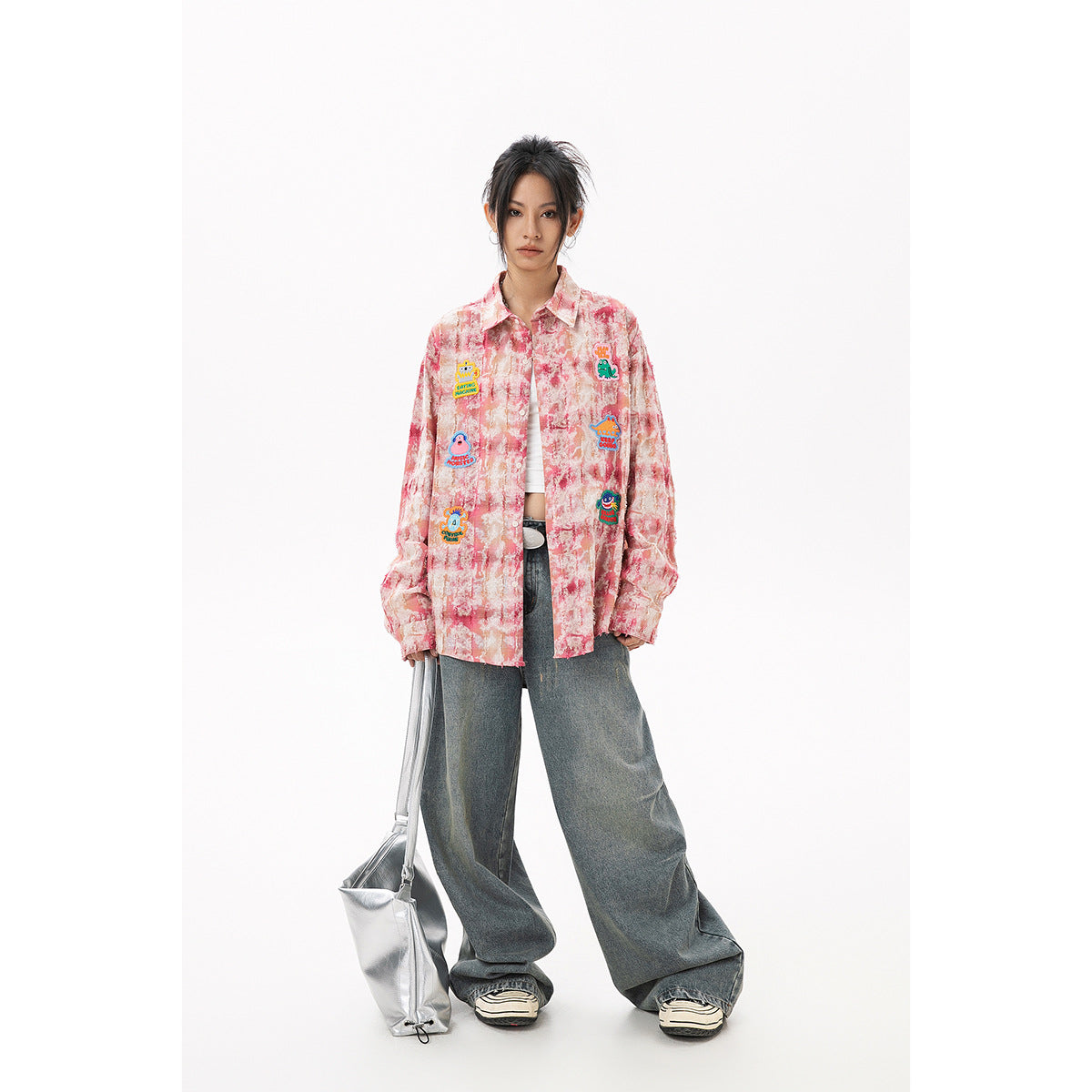 Model wearing an untucked pink marbled button-up shirt with colorful cartoon patches and wide-leg jeans.