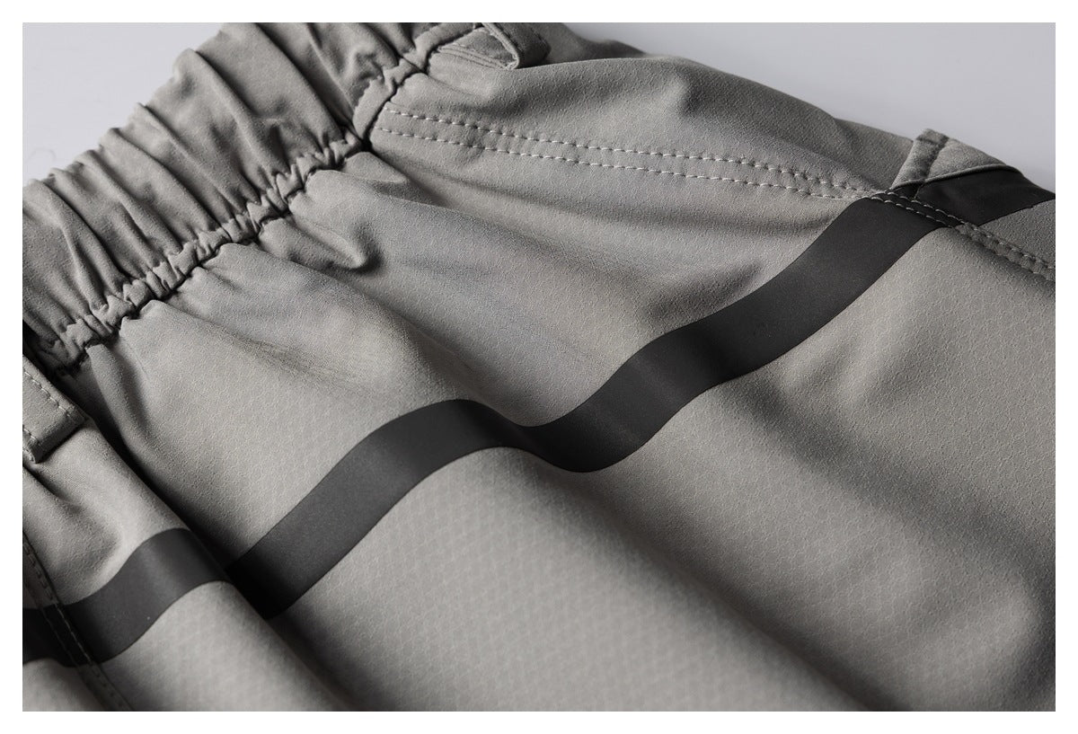 Close-up of gray garment fabric with a gathered elastic edge, stitched seams, and a broad black stripe.