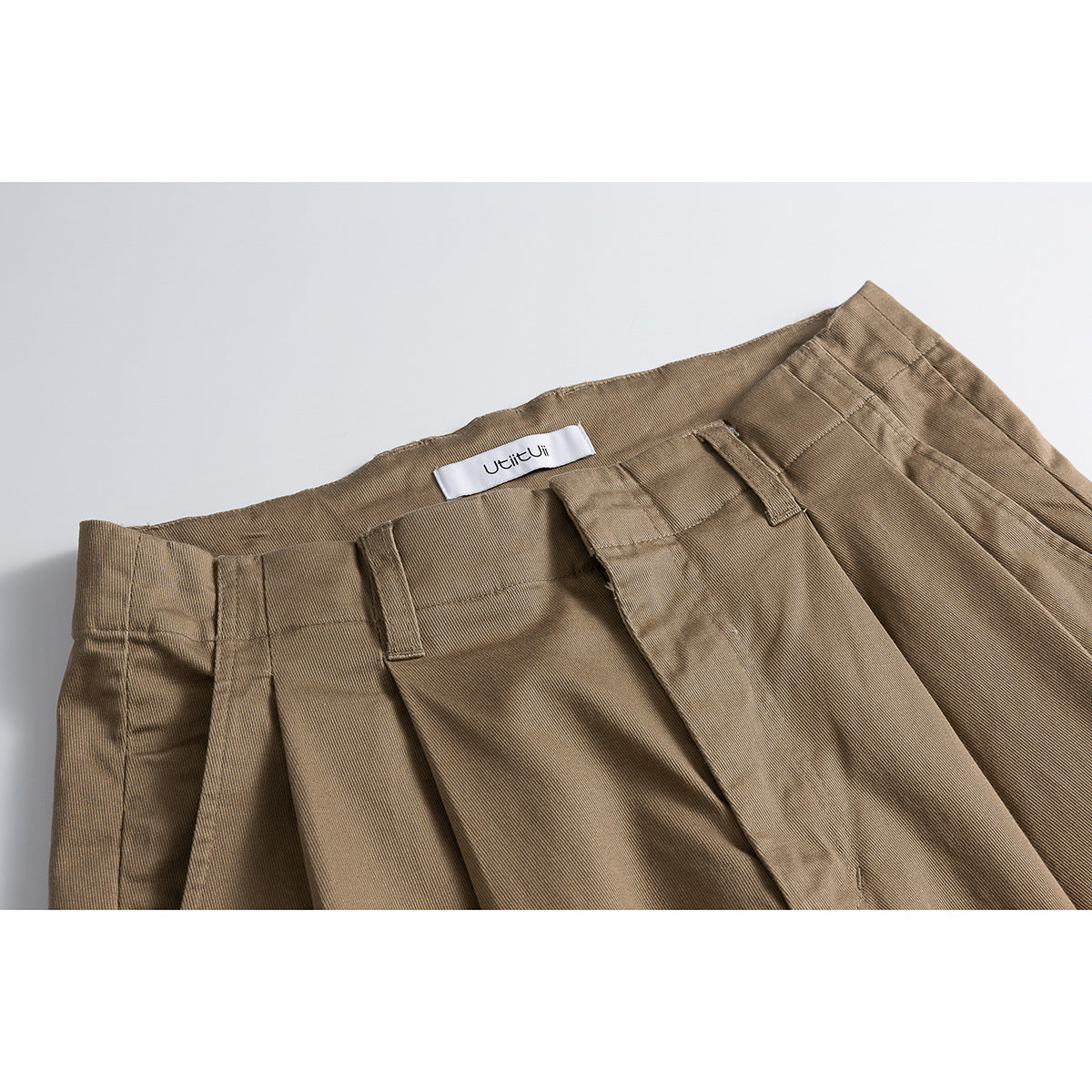 Close-up of tan wide-leg shorts showing the waistband, belt loops, pleats and sewn-in label.