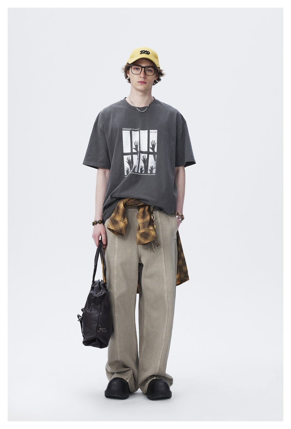 Full-length front view of a model wearing an oversized charcoal graphic T-shirt and loose beige trousers.