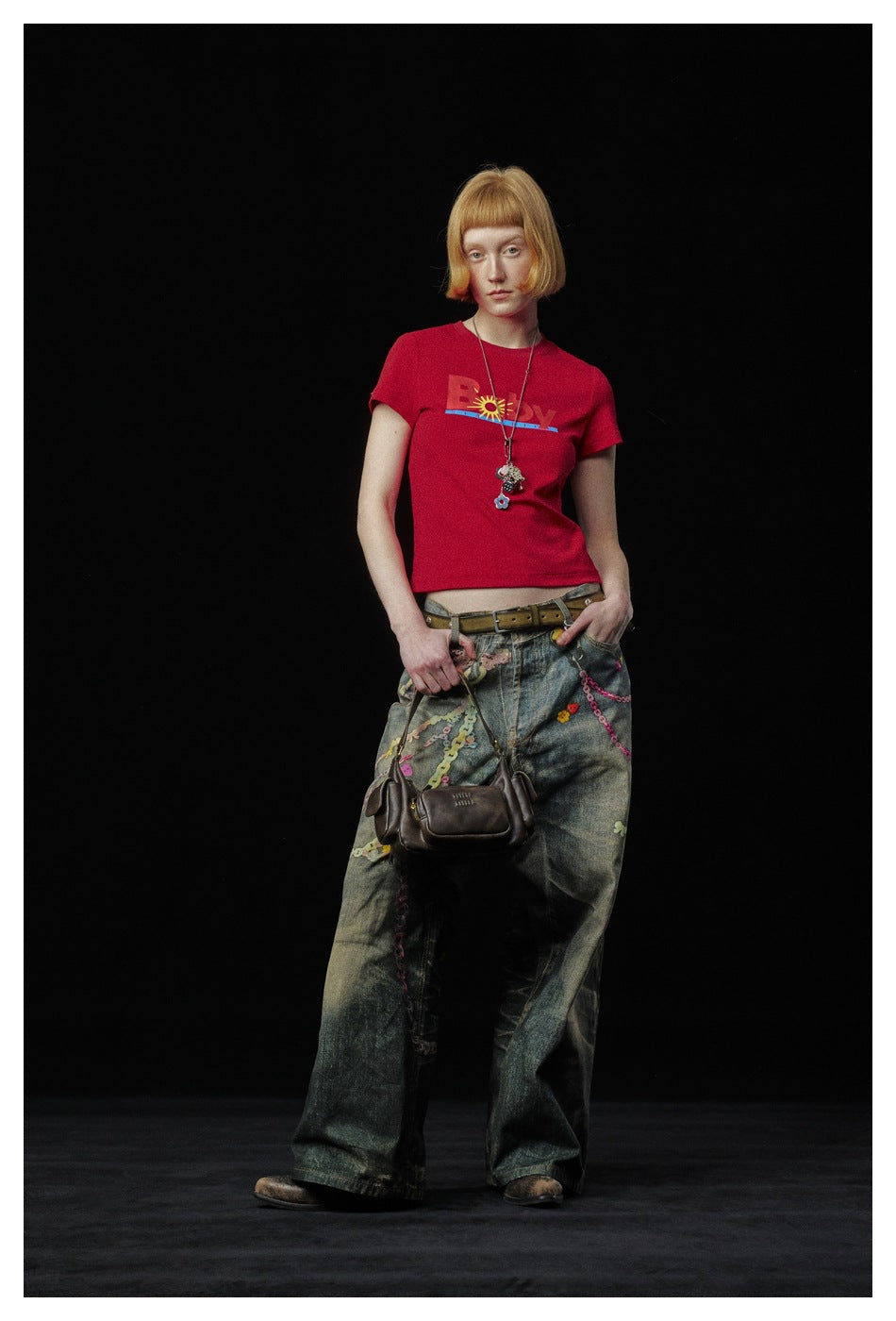 Model in the red cropped graphic T-shirt with low-rise wide-leg jeans and a brown shoulder bag, three-quarter pose