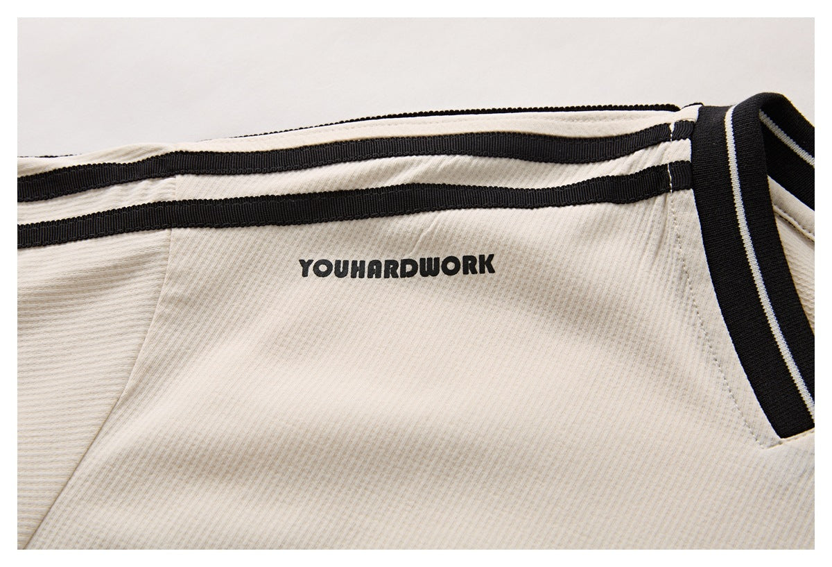 Close-up of the ivory shirt’s black shoulder stripes and printed black text near the shoulder.