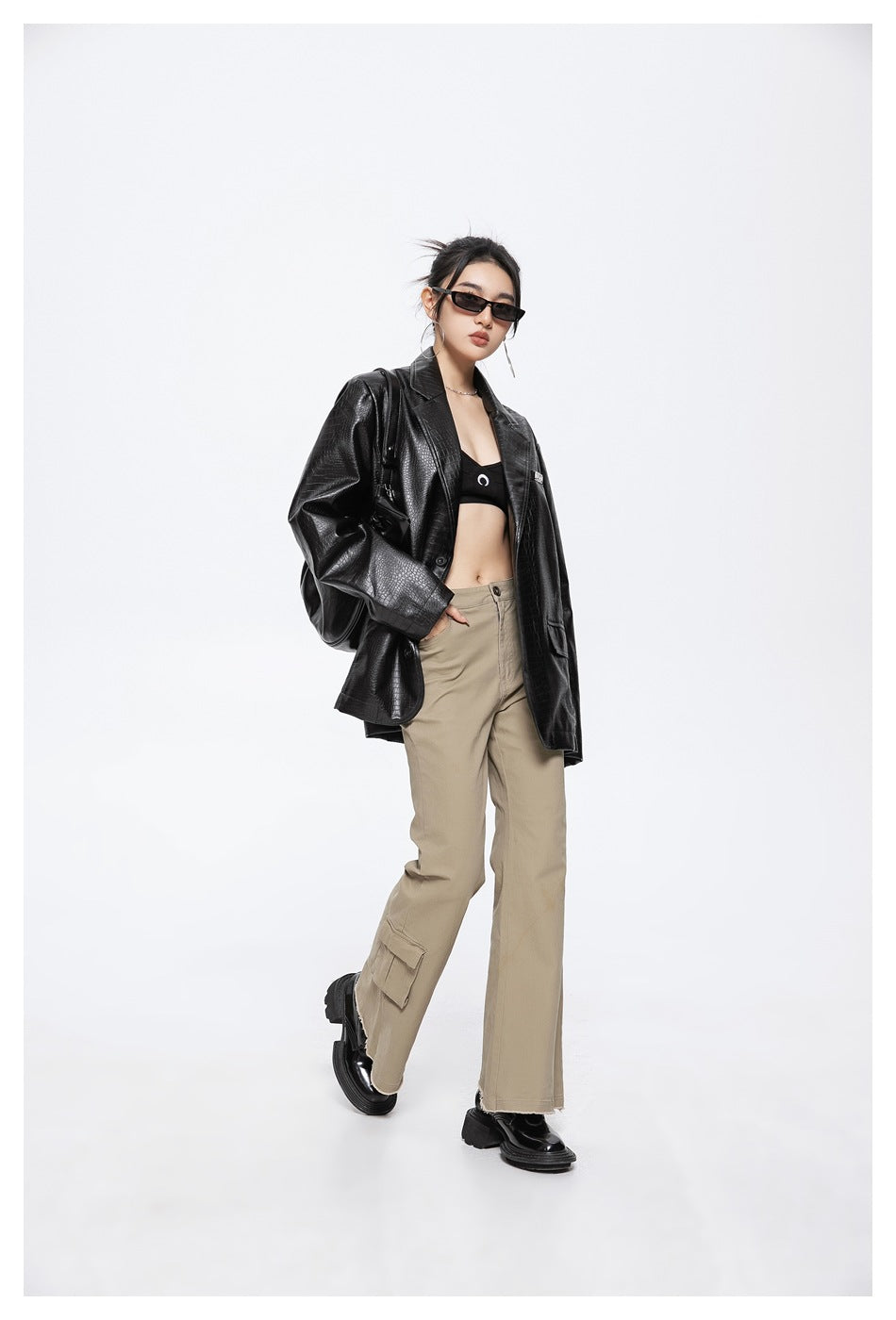 Model wearing an oversized black crocodile-textured blazer with beige cargo trousers, shown at a slight angle.